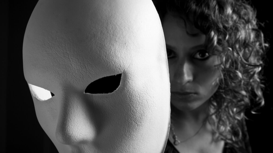 Young woman reveals her face behind white mask.